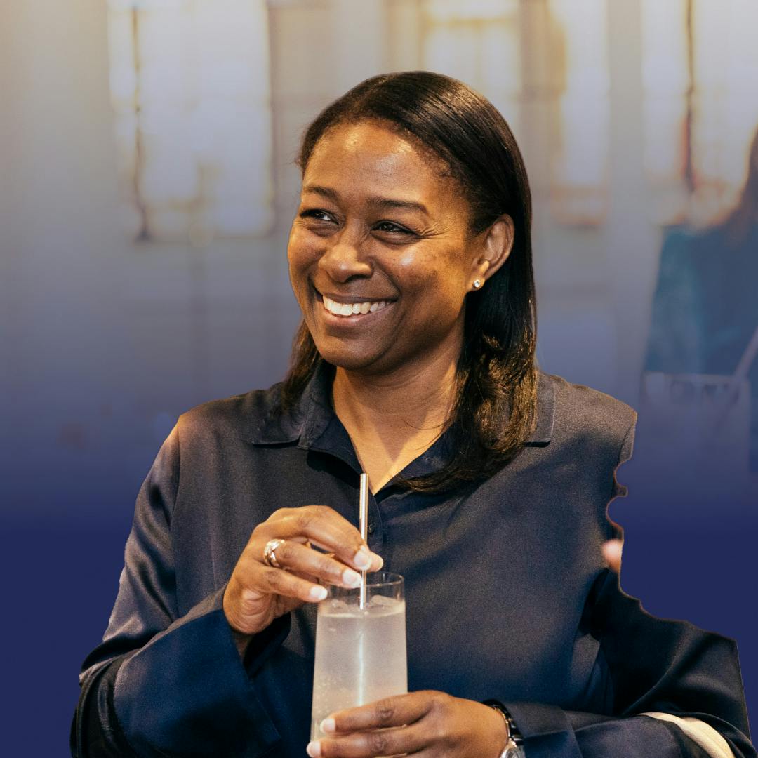 A smiling woman in a navy top holding a drink in a glass with a straw
